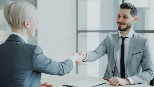 Two professionals shaking hands across a desk after a job interview