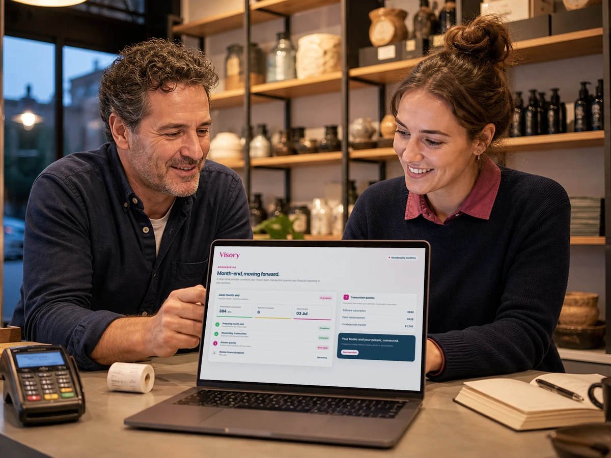 Two retail colleagues review month end figures on a laptop at a shop counter.