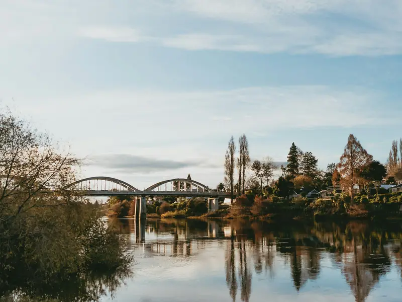 The Fairfield Bridge over the Waikato River in Hamilton, with autumn trees reflected in the water.