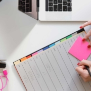 A woman prepare to write on a pink post-it note while at her desk.