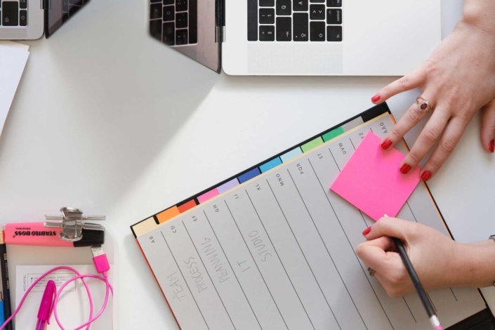 A woman prepare to write on a pink post-it note while at her desk.