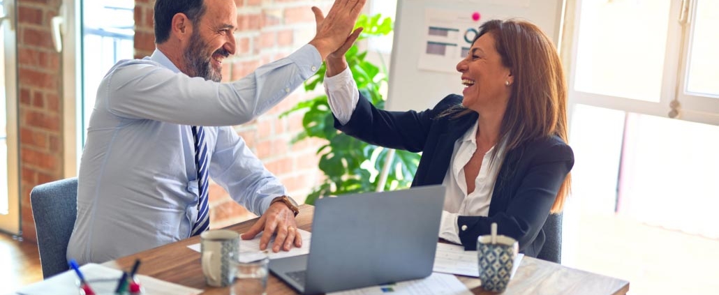 Two middle age employees celebrate a business success with a high five.