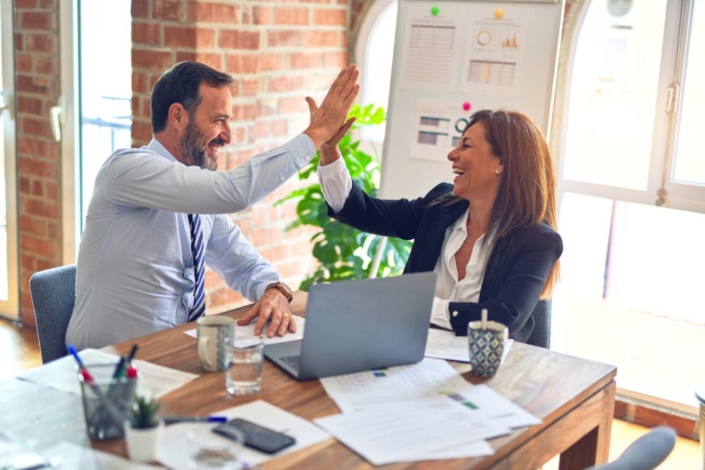 Two middle age employees celebrate a business success with a high five.