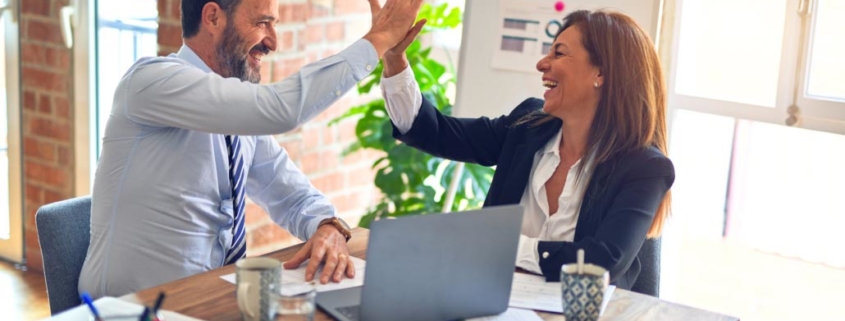 Two middle age employees celebrate a business success with a high five.