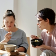 a support worker sitting with a young woman eating breakfast