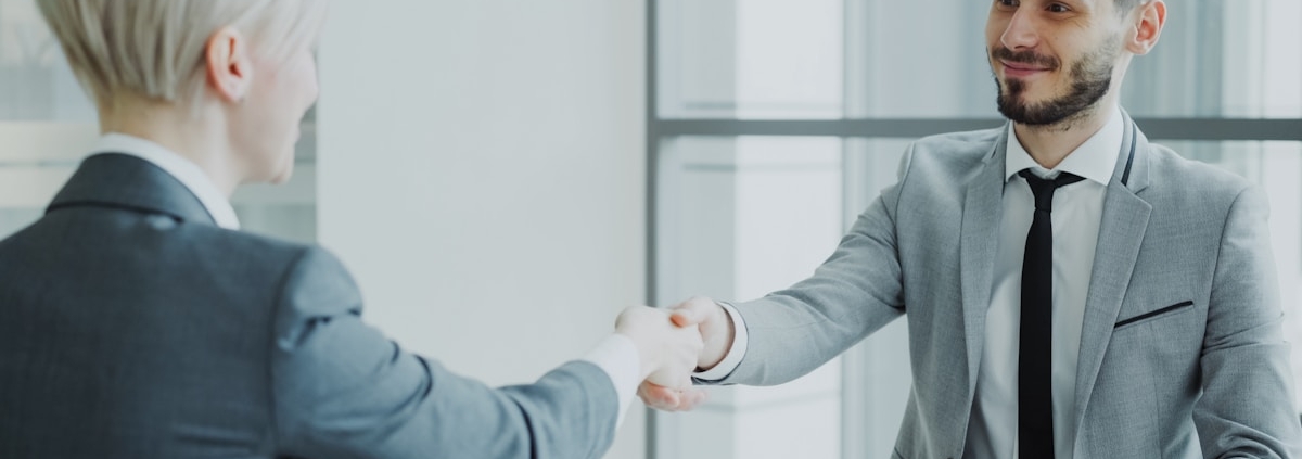 Two professionals shaking hands across a desk after a job interview